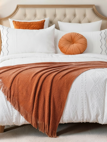 Bed with white bedding, orange throw blanket, and pillows in a bedroom setting.