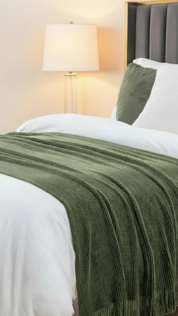 Green blanket on a bed with a lamp in the background