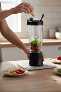 Person preparing a smoothie with a blender on a kitchen counter.