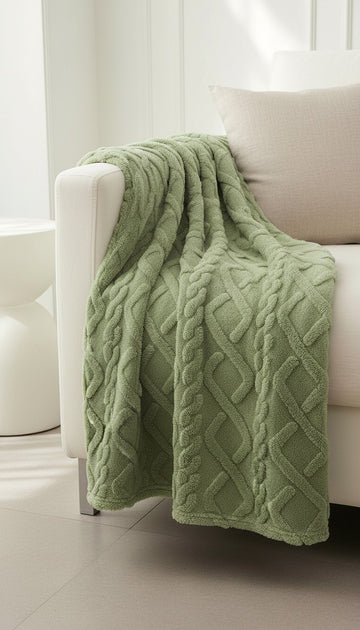 Green cable knit blanket draped over a white chair in a bright room.