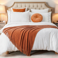 Neatly made bed with white bedding, orange throw blanket, and pillows in a bedroom setting.